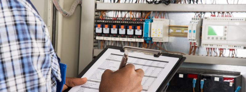Close-up Of Male Technician Writing On Clipboard In Front Of Fusebox